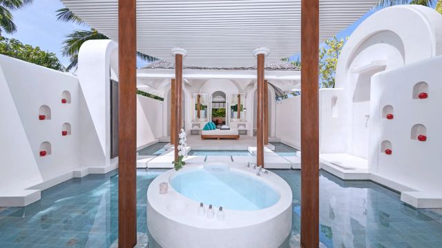 Luxuriöses Outdoor-Badezimmer einer Villa mit freistehender Badewanne, türkisfarbenem Wasser, weißem Design und Holzsäulen im Anantara Kihavah Maldives