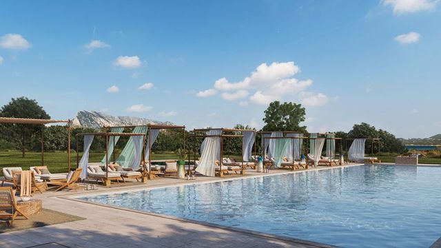 Der elegante Poolbereich des Baglioni Resort Sardinia bietet stilvolle Daybeds mit weißen Vorhängen, Blick auf grüne Hügel und eine entspannte Atmosphäre unter freiem Himmel.