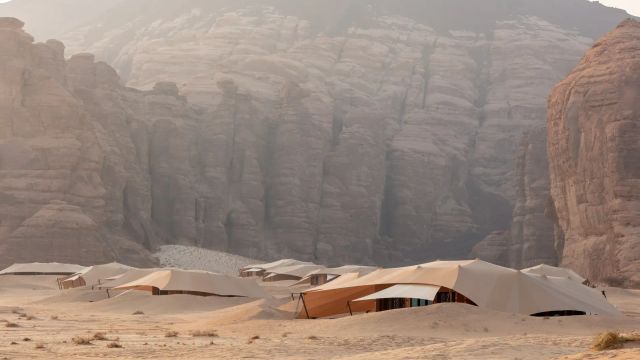 Luxuriöse Wüstenzelte des Banyan Tree AlUla Resorts eingebettet in die sandige, von mächtigen Sandsteinfelsen umgebene Landschaft von AlUla, Saudi-Arabien – in warmem Morgenlicht, das die dramatische Kulisse weich durchleuchtet.