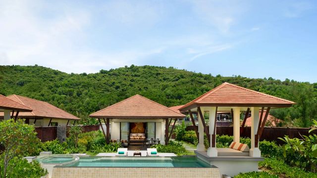Tropische Villa des Banyan Tree Lang Co Resorts in Vietnam mit privatem Pool, offenen Pavillons und traditionellen Ziegeldächern, eingebettet in üppig grüne Natur und umgeben von bewaldeten Hügeln unter klarem, blauem Himmel.
