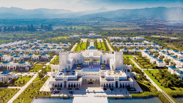 Majestätisches Gebäude im maurischen Stil im Banyan Tree Tamouda Bay, gespiegelt in einem ruhigen Infinity-Pool, umgeben von Palmen und luxuriöser Resort-Atmosphäre bei strahlend blauem Himmel.