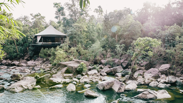 Luxus-Safarizelt am Flussufer umgeben von dichtem Wald und großen Felsen
