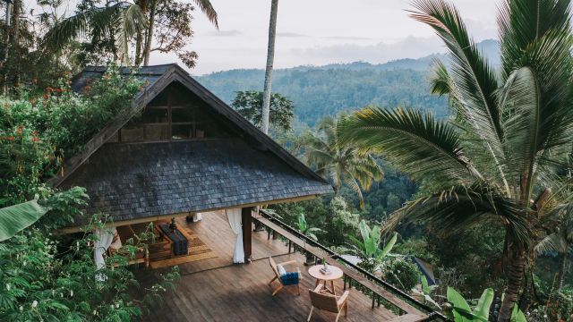Offene Luxusvilla im Dschungel des Buahan, a Banyan Tree Escape Resorts auf Bali, mit Holzdeck, traditionellen Materialien und atemberaubendem Blick auf dichte tropische Wälder und Palmen unter einem leicht bewölkten Himmel.