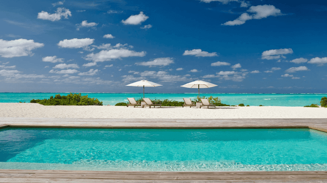 Vor Ihnen liegt ein eleganter privater Pool, dessen kristallklares Wasser perfekt das Blau des Himmels reflektiert. Dahinter erstreckt sich ein makelloser Sandstrand.