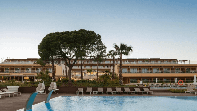 Der wunderschöne Poolbereich im EPIC SANA Algarve lädt alle Gäste zum Entspannen und Aktiv sein ein - das Hotel im Hintergrund mit seinen Zimmern und Suiten.
