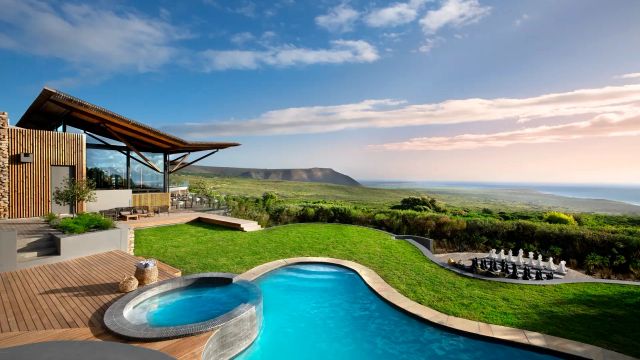 Luxuslodge Grootbos in Südafrika mit modernem Design, privatem Pool, Whirlpool, Rasenfläche mit XXL-Schachspiel und Panoramablick auf grüne Hügel und das Meer.