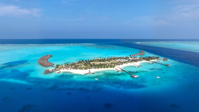 Luftansicht einer tropischen Insel mit luxuriösen Bungalows über klarem türkisfarbenem Wasser.