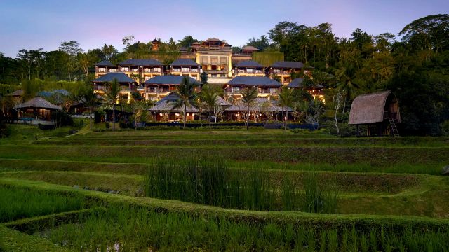 Abendaufnahme des Mandapa, a Ritz-Carlton Reserve in Ubud, Bali, mit traditioneller balinesischer Architektur, eingebettet in üppige Natur und umgeben von malerischen Reisfeldern.