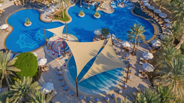Qasr Al Sarab Desert Resort By Anantara großer Kids Pool mit Liegestühlen und Sonnenschutz umgeben von Palmen