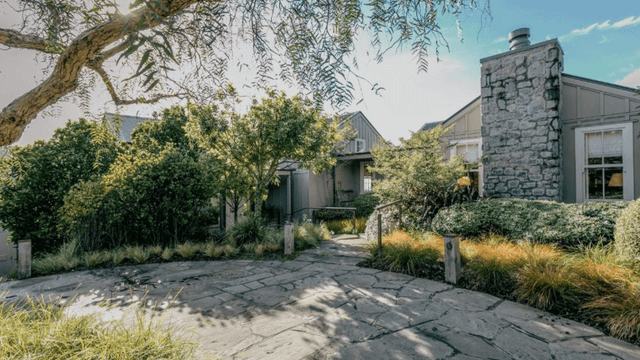 Elegante Cottages des Rosewood Cape Kidnappers mit gemütlichen Rattansesseln, umgeben von naturbelassener Bepflanzung und Blick auf bewaldete Hügel in idyllischer, ländlicher Umgebung.