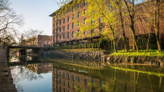 Backsteingebäude des Rosewood Washington, D.C., malerisch am historischen C&O Canal gelegen, umgeben von Bäumen und mit ruhiger Wasserreflexion.
