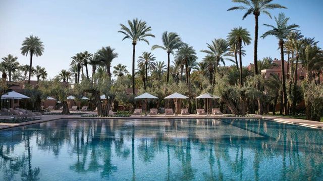 Das Royal Mansour Marrakech mit Blick auf einen großen, eleganten Pool mit glasklarem Wasser, umgeben von Sonnenliegen und weißen Sonnenschirmen.
