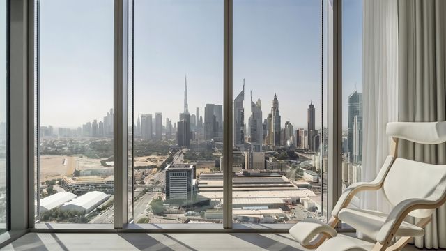 Innenansicht eines stilvollen Hotelzimmers im SIRO One Za’abeel Dubai mit weißem Designerstuhl vor einer bodentiefen Fensterfront und Panoramablick auf Dubais Skyline, einschließlich Burj Khalifa.