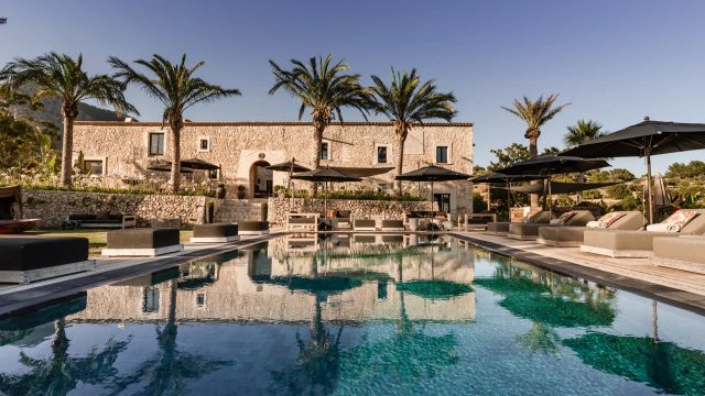 Luxuriöse Finca des Hotels Spirit of Son Fuster auf Mallorca mit Natursteinfassade, Palmen und stilvoller Poolanlage unter klarem Himmel.