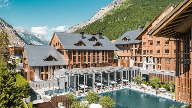 Luxuriöses Alpenresort The Chedi Andermatt mit moderner Holzarchitektur, großzügigem Poolbereich und Blick auf die umliegende Berglandschaft.