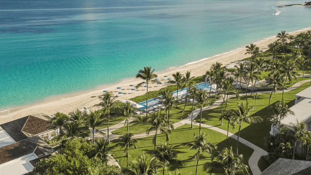 Im Vordergrund glitzert ein einladender Pool, der nahtlos mit der untergehenden Nachmittagssonne spielt. Dahinter verläuft ein makelloser Sandstrand, an den sanfte Wellen des kristallklaren Meers schlagen.