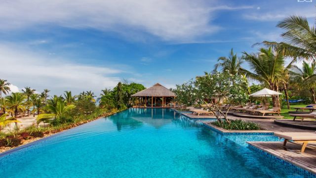 Weitläufiger Infinity-Pool im ZURI Zanzibar mit Holzdeck, tropischer Bepflanzung und Blick auf den weißen Sandstrand und das türkisfarbene Meer.