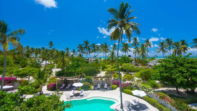 Tropische Gartenanlage des Zanzibar White Sand Luxury Villas & Spa mit Lagunenpool, üppiger Vegetation und Blick auf den Indischen Ozean.
