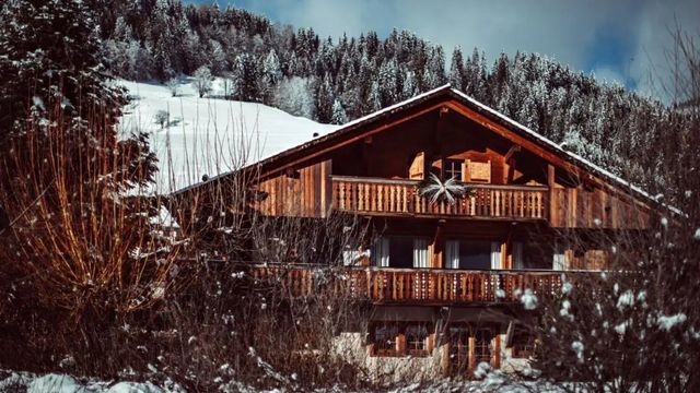 Gehobene Berghütte aus Holz mit verschneiten Tannen im Hintergrund