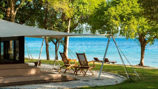 Sitzbereich am Strand mit Blick auf das blaue Meer und grüne Bäume.