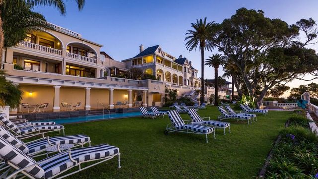 Elegantes Hotelgebäude bei Abenddämmerung mit Rasen und Liegestühlen.