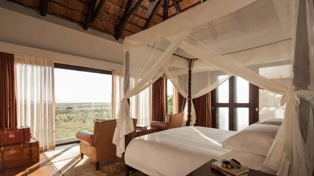 Geräumiges Schlafzimmer mit baldachinüberzogenem Himmelbett und Blick auf die Serengeti.