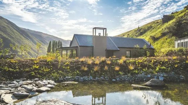Lodge umgeben von Natur und grünem Hügel, reflektiert in einem Teich