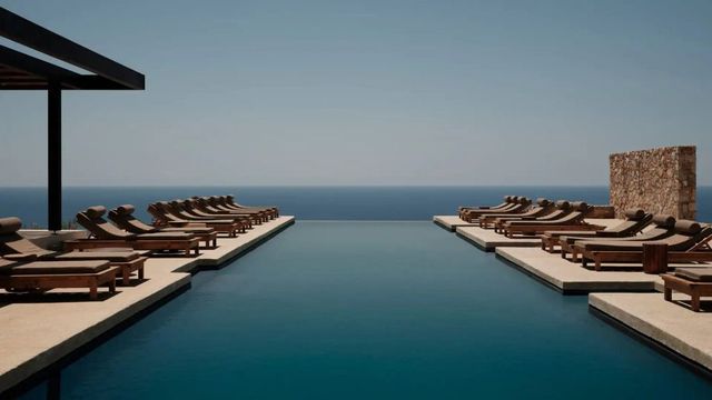 Infinity Pool mit Liegestühlen unter klarem Himmel und Blick auf das weite Meer