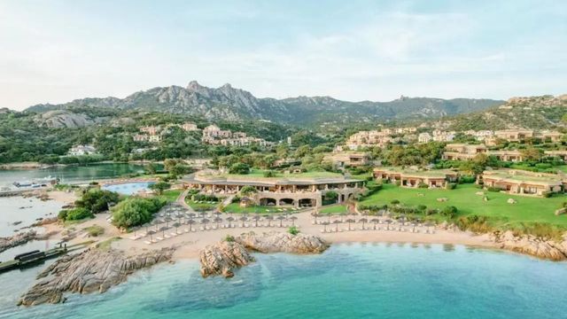 Panoramablick auf das Hotel Pitrizza entlang der Küste mit Strand und Bergen.