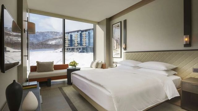 Helles Hotelzimmer mit großem Bett und Winterlandschaft im Hintergrund.