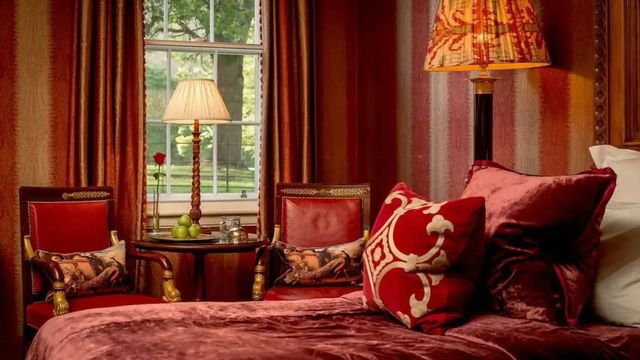 Gemütliche Sitzecke mit rotem Samt und dekorativen Kissen vor einem Fenster.