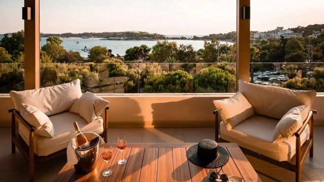 Terrasse mit Blick auf das Meer, ausgestattet mit Holztisch, Sesseln und Champagner.