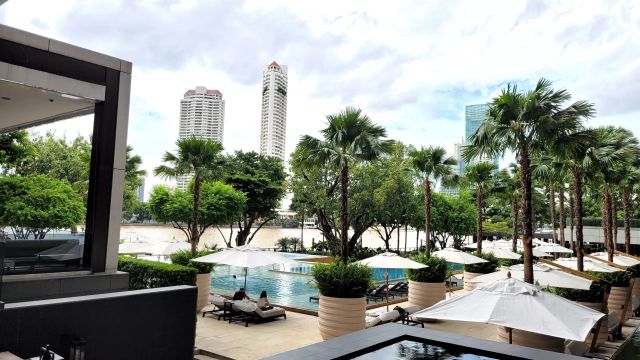 Four Seasons Bangkok Außenbereich mit Pool, Palmen und Blick auf Skyline Gebäude
