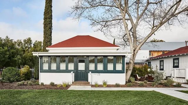 Charmante historische Hütte mit rotem Dach und grünen Akzenten vor gepflegtem Rasen