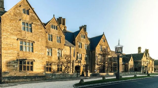 Historische Fassade des Lygon Arms Hotels aus sandfarbenem Stein im Sonnenlicht.