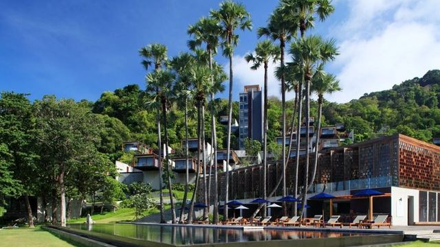 Infinity-Pool umgeben von Palmen mit Blick auf Hügel und Meer bei The Naka Phuket.