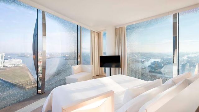 Lichtdurchflutetes Zimmer mit Doppelbett und Panoramafenstern mit Blick auf Hamburg