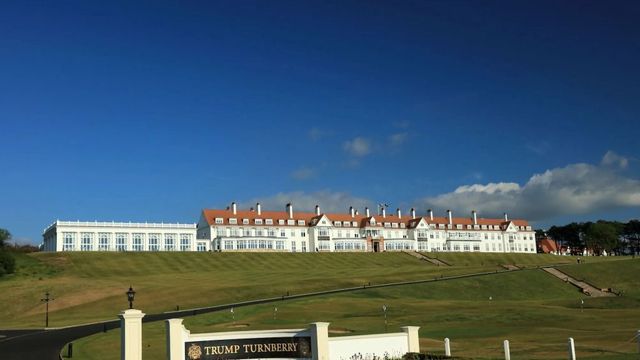 Weitläufiger Blick auf das Trump Turnberry Hotel vor blauem Himmel.