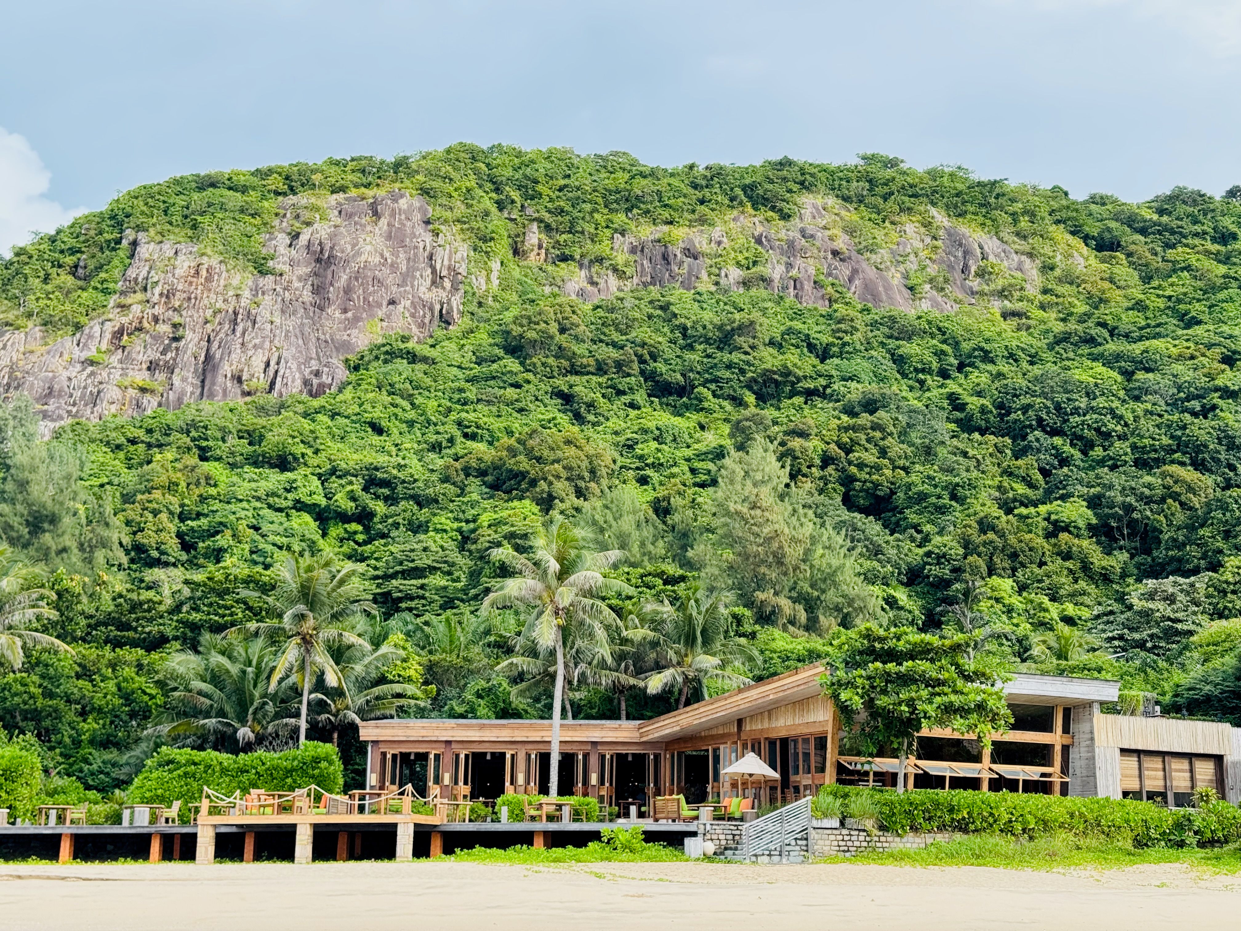 Große auf Holzrahmen gebaute Strandvilla vor üppiger grüner Felsenlandschaft