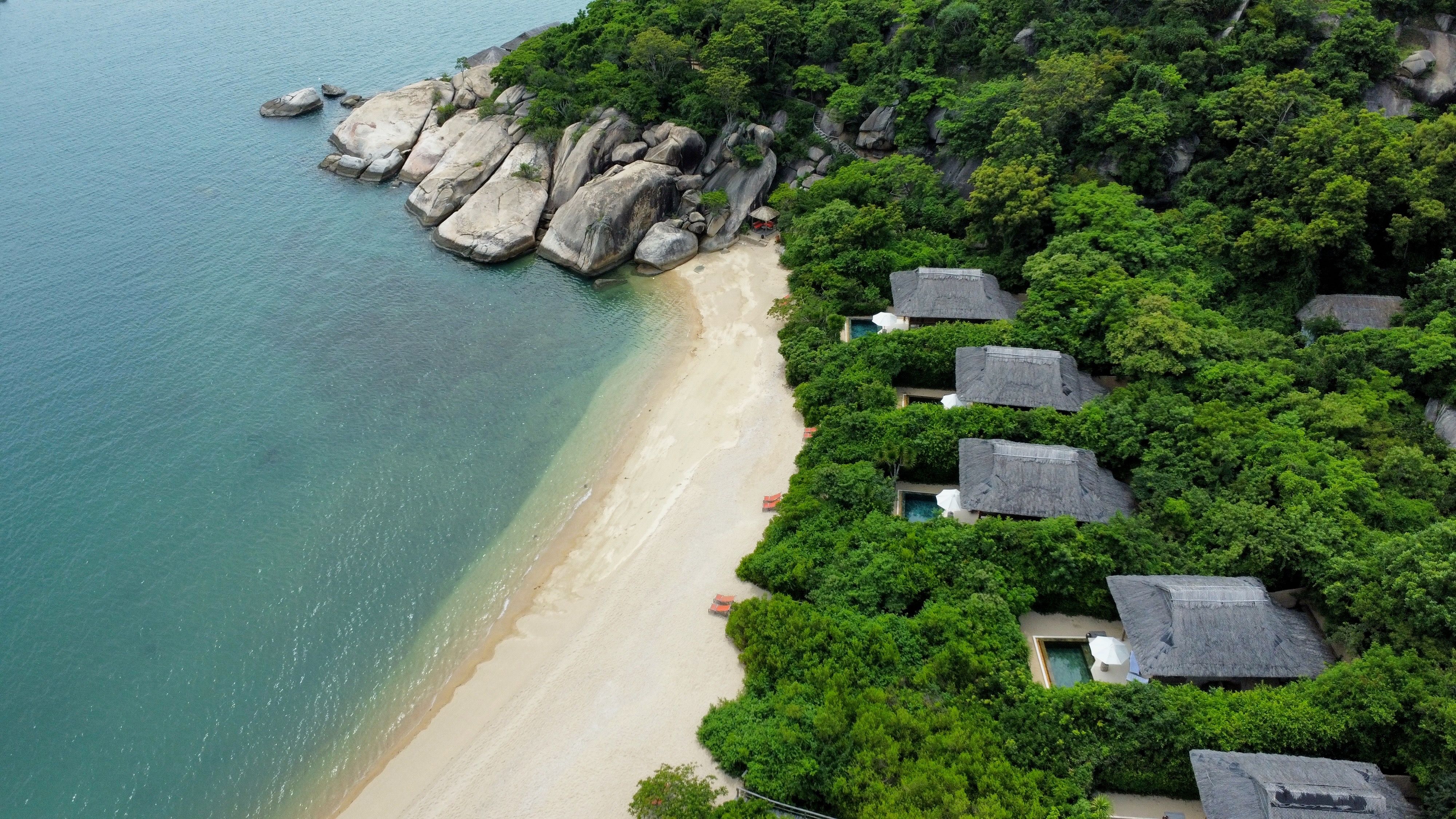 Luftaufnahme eines Ferienresorts an einer einsamen Bucht mit Sandstrand und Wald.