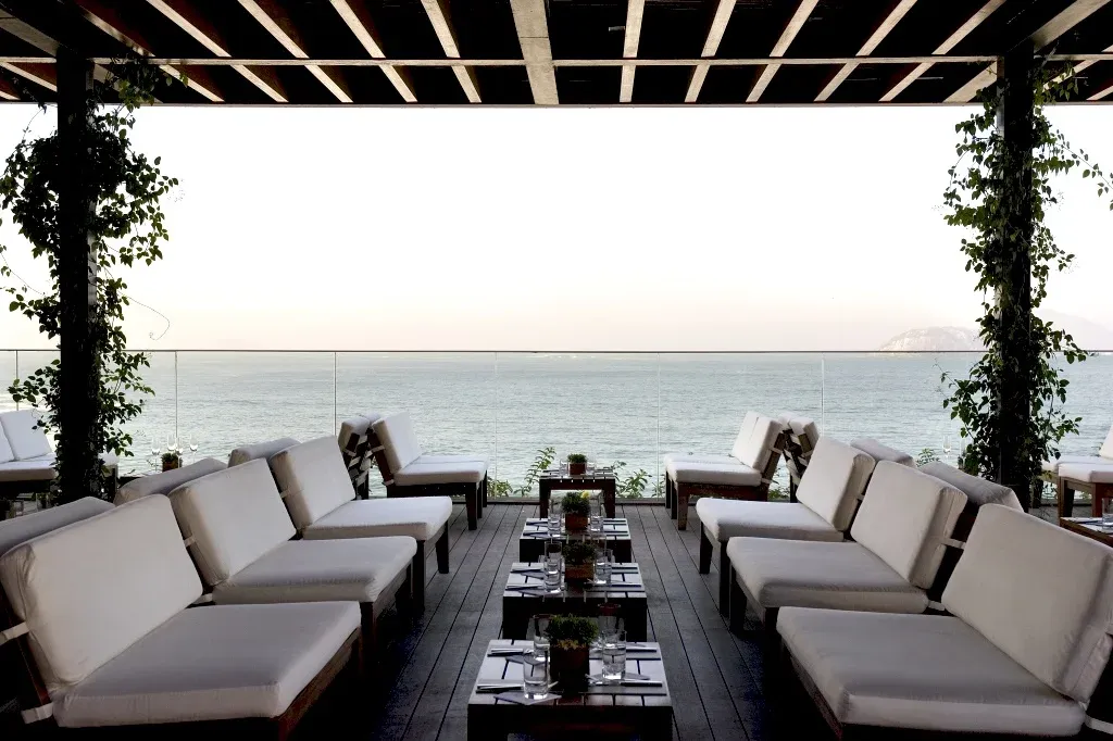 Terrasse mit weißen Sofas und Meerblick unter Holzdach mit grünem Bewuchs