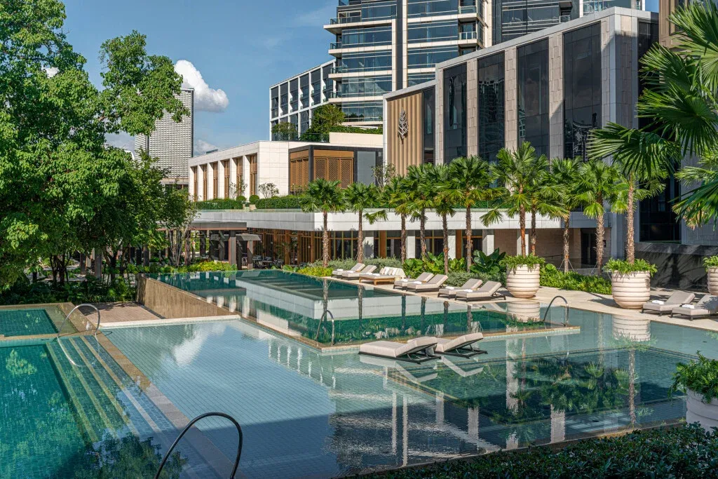 Luxuriöser Hotelpool mit Liegen umgeben von Grünflächen und moderner Architektur.