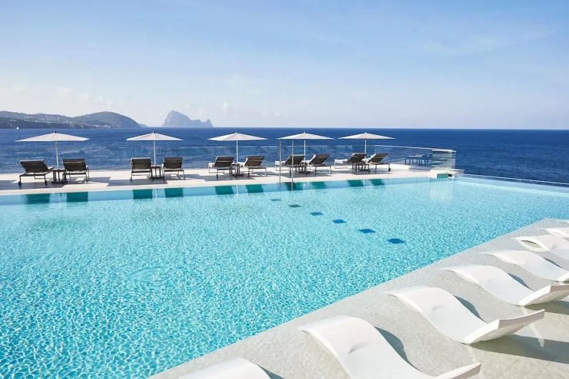 Infinity-Pool im 7Pines Resort Ibiza mit Sonnenliegen und traumhaftem Blick auf das Mittelmeer und die Insel Es Vedrà.