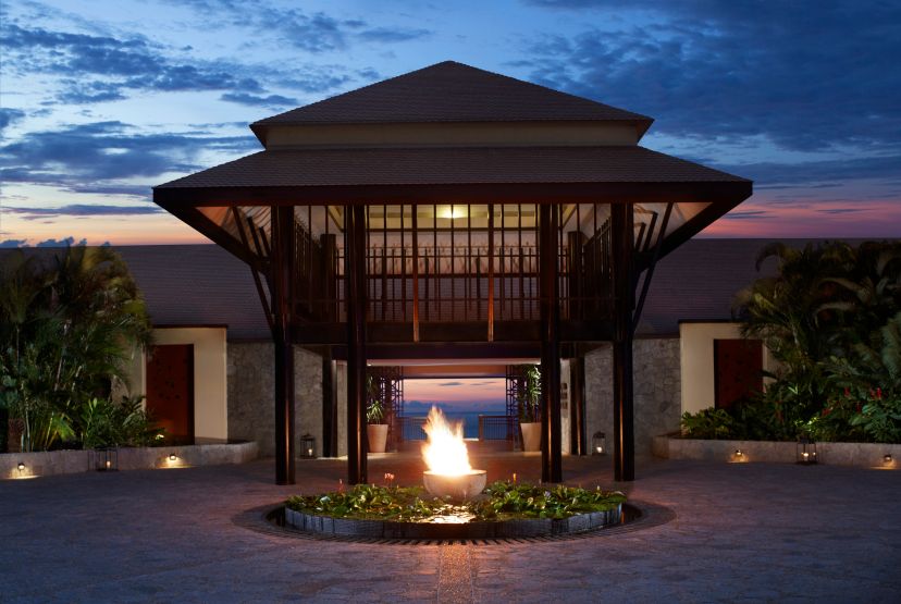 Ein stilvoll beleuchteter Eingangsbereich des Banyan Tree Cabo Marqués bei Sonnenuntergang, mit modernem Pavillon, tropischer Bepflanzung und einem flackernden Feuerbecken – die perfekte Einstimmung auf einen luxuriösen Aufenthalt.