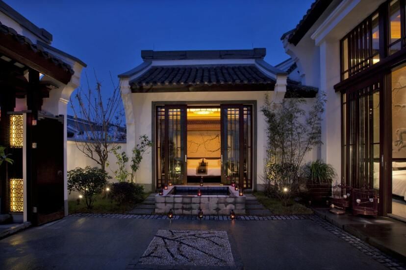 Elegante Villa im Banyan Tree Hangzhou bei Nacht, mit traditioneller chinesischer Architektur, beleuchteten Laternen, filigranen Holzelementen und einem kleinen Hofgarten im Innenbereich.