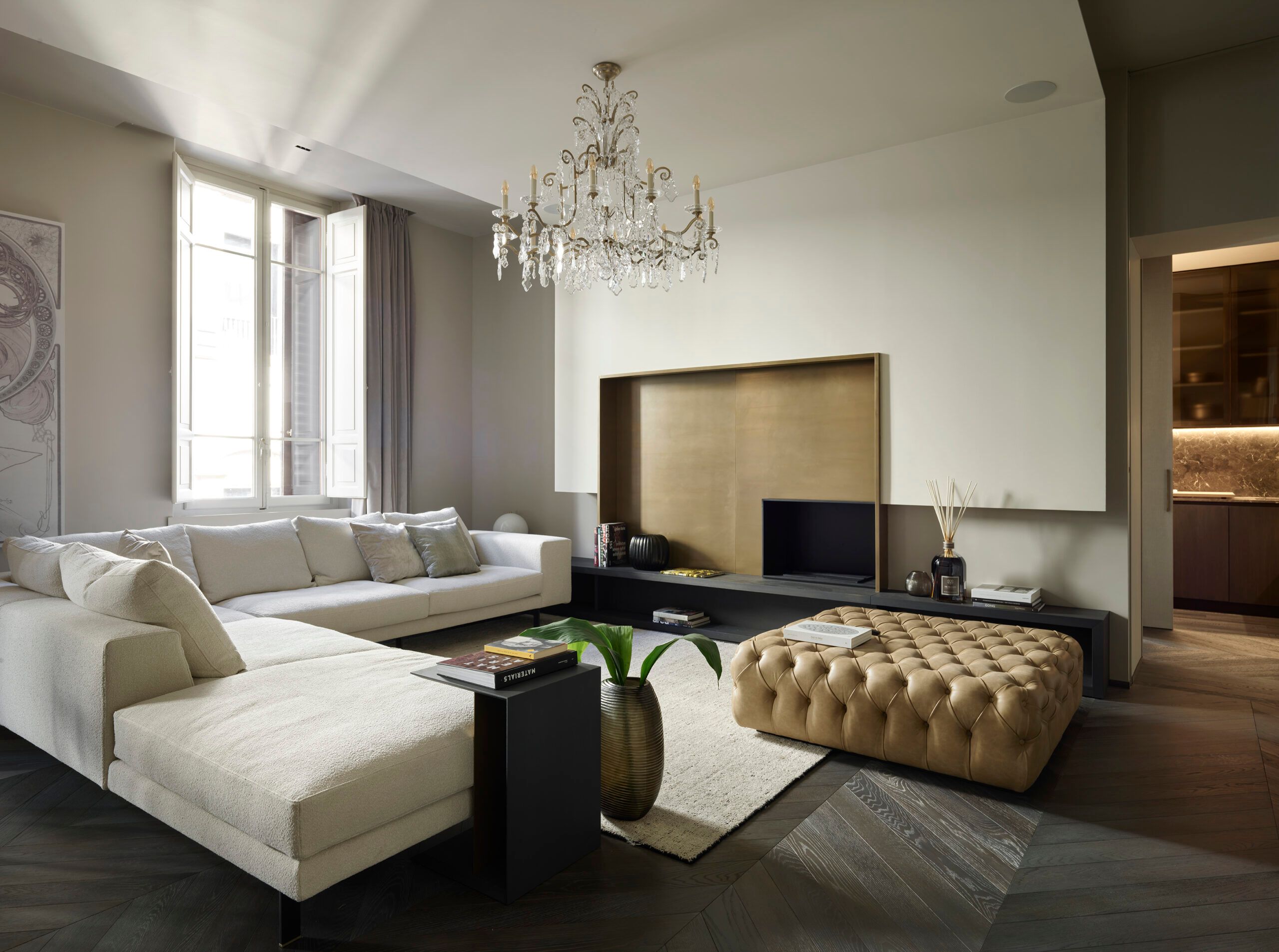 Elegantes Wohnzimmer einer Suite in den ETRA Suites mit cremefarbenem Sofa, Kristallluster, goldener Wandnische, gepolstertem Hocker und modernen Designelementen in warmen Naturtönen.