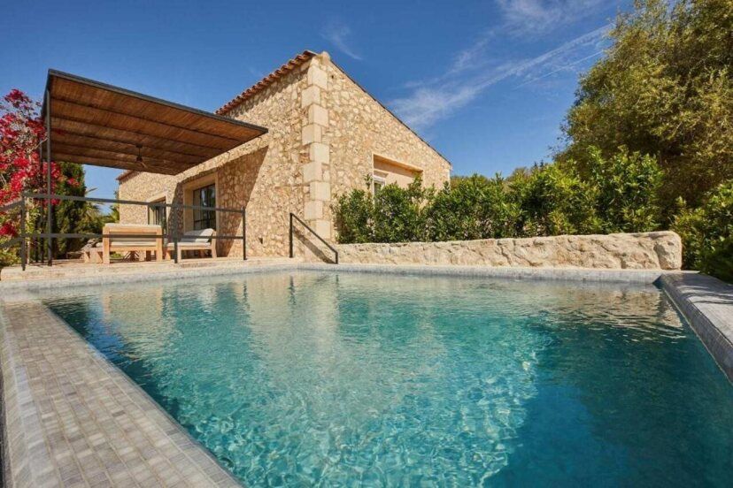 Natursteinvilla der Finca Serena Mallorca mit privatem Pool, überdachter Terrasse und mediterranem Garten bei strahlend blauem Himmel – ein Rückzugsort in ruhiger, ländlicher Umgebung.