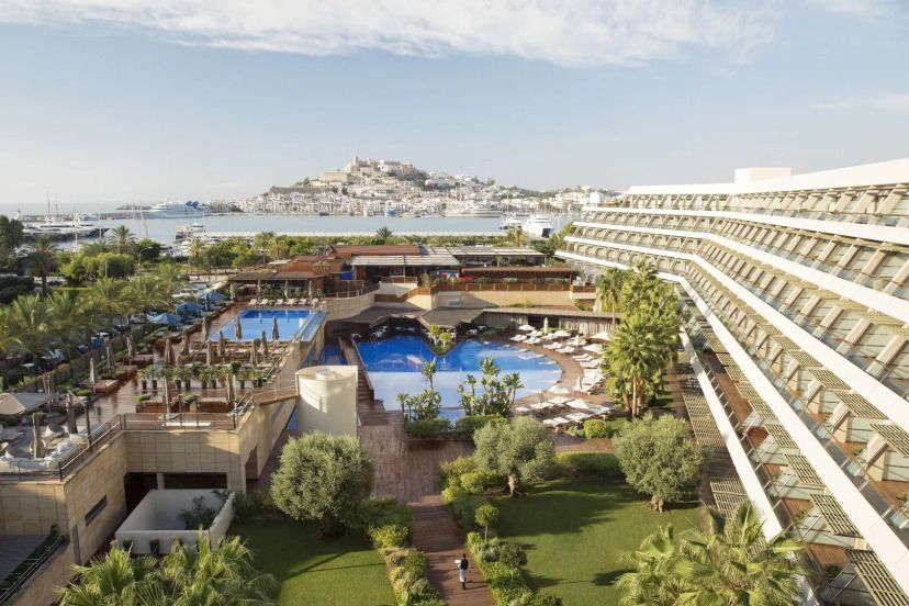 Luxuriöse Hotelanlage mit zwei Pools, viel Grünfläche und Blick auf die Altstadt von Ibiza und den Yachthafen.