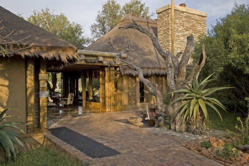 Eingangsbereich der Jabulani Safari Lodge mit traditionellem Reetdach, Natursteinmauer, rustikaler Holzarchitektur und umliegender afrikanischer Vegetation – harmonisch eingebettet in die Wildnis.