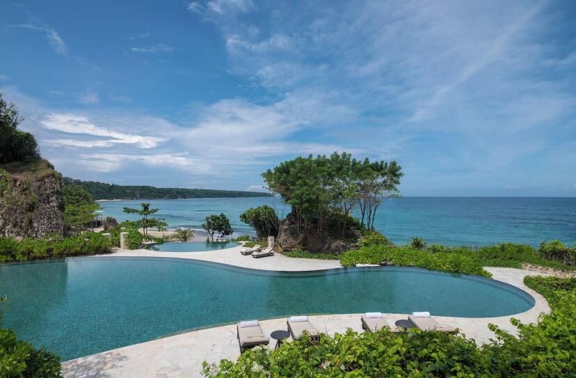 Infinity-Pool des Jumeirah Bali mit Blick auf den Indischen Ozean, umgeben von tropischem Grün, Felsen und eleganten Sonnenliegen – luxuriöse Oase inmitten balinesischer Naturkulisse.